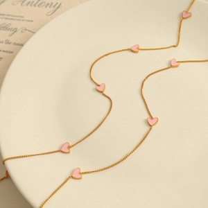 Elegant gold chain necklace with pink enamel heart charms on a white display tray