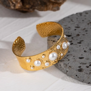 Golden hammered stainless steel open bangle with inlaid pearls on a textured stone base