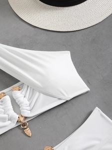 Close-up of white ribbed bikini top featuring elegant gold metal chain and floral pendant