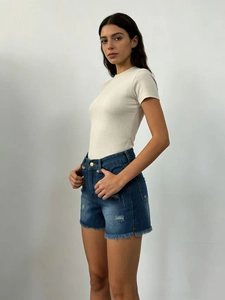 Détail d'un short en jean taille haute effiloché et d'un t-shirt beige en maille côtelée