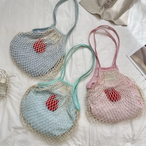 Dettaglio di borse a rete intrecciata blu, verde e rosa con cuori rossi in peluche