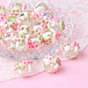 Close-up of clear acrylic beads with pink mushroom motifs in a glass dish with lace