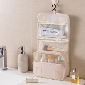 Hanging beige travel toiletry bag with multiple compartments in a modern bathroom