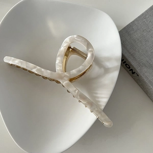 Close-up of a white marble acetate hair claw clip with twisted design on ceramic tray