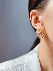 Macro view of gold flower earrings with white zircon petals on woman's earlobe