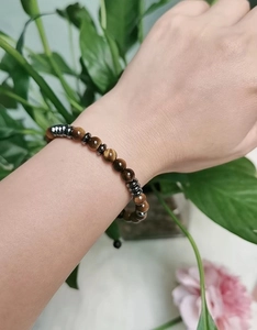 Close-up of Morse code tiger eye stone bracelet worn on wrist with natural plant background