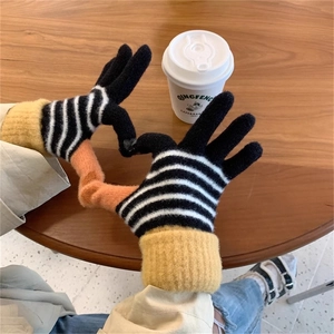 Close-up of striped touch screen knit gloves in a cozy cafe setting with heart hand gesture