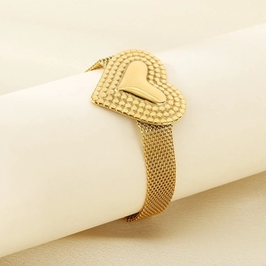 Detail of a golden heart bracelet featuring a mesh metal strap on a cylindrical stand