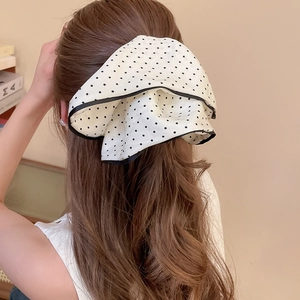 Detail of a large white polka dot silk bow hair clip worn on a low ponytail