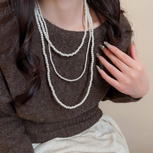 Dettaglio di una collana di perle bianche multistrato su un maglione marrone