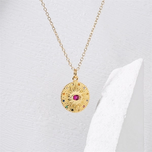 Macro view of gold Evil Eye pendant with red center stone and colorful crystals