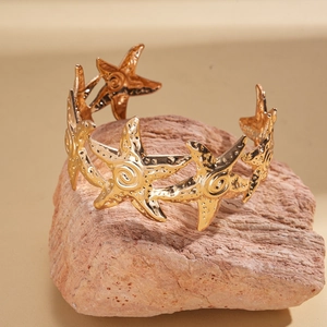Detail of a gold open cuff bracelet featuring an intricate cutout starfish design