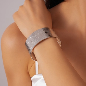 Detailed close-up of a wide silver cuff bracelet with intricate floral engraving patterns