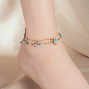 Double-layered gold anklet with star charms and blue beads on a warm fabric background