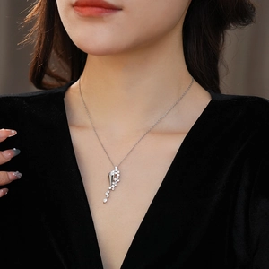 Close-up of silver hourglass pendant with white zircon inlays on an asymmetric tassel necklace
