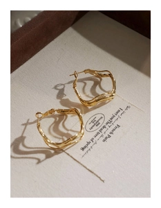 Detailed view of golden irregular twisted hoop earrings on an elegant display card