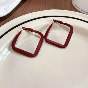 Détail des créoles carrées floquées rouge foncé sur un plateau à bijoux en céramique