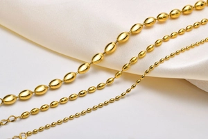 Detailed view of three different sizes of golden oval bead chains on white satin fabric
