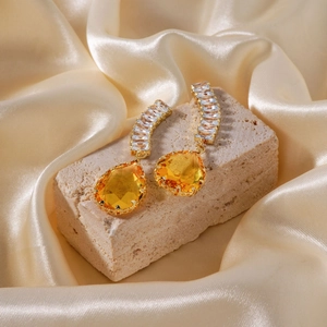 Detailed shot of teardrop yellow gemstone earrings on beige stone and champagne silk