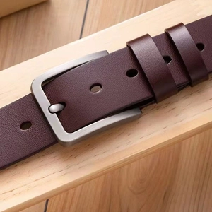 Classic men's brown leather belt with silver metal pin buckle on light wood background