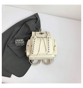 Flat lay of cream PU leather backpack with cross rivets and drawstring closure detail
