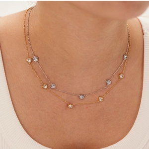 Detailed view of two-tone heart pendant necklace with bezel-set zircons on woman neck