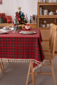 Close-up of red plaid Christmas tablecloth with beige fringe tassels and cotton texture
