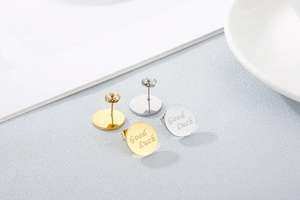 Detailed shot of round gold and silver stud earrings engraved with Good Luck text