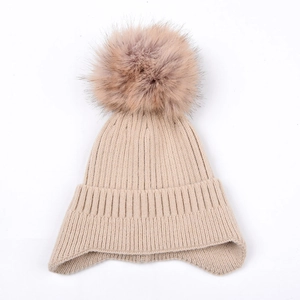 Detail showing beige ribbed knit texture and soft faux fur pompom on winter beanie hat