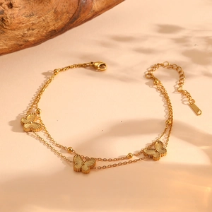 Détail d'un bracelet double couche doré avec papillons et petites perles sur fond beige