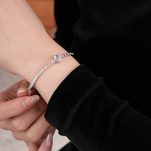 Macro detail of silver zircon bangle with oval center stone on a black velvet sleeve