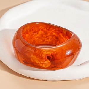 Macro shot of an amber resin geometric bangle with marbled texture on a minimalist tray