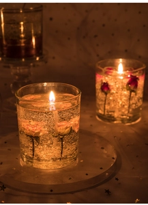 Close-up of a clear jelly candle in glass with embedded yellow roses and warm lighting