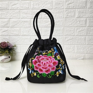 Detail of colorful peony embroidery and drawstring closure on a black canvas bucket bag