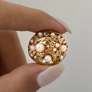 Detailed close-up of a vintage gold ring with colorful crystals and white pearls