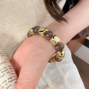Close-up of geometric gold cubes and sparkling dark stone beads on a stretch bracelet