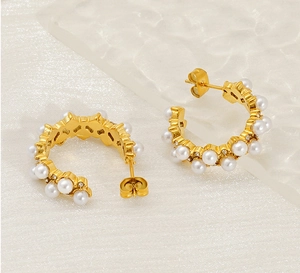 Close-up of golden C-shaped hoop earrings featuring inlaid pearls and sparkling crystals