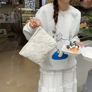 Close-up of cream floral quilted makeup bag held by hand in a lifestyle bakery setting
