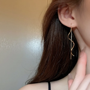 Detail of elegant gold wave tassel threader earrings worn on model for stylish look