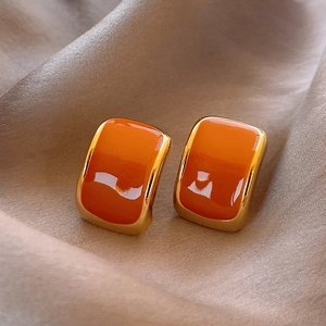 Close-up of square orange enamel earrings with gold trim on champagne silk fabric