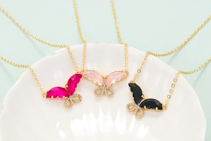 Detailed close-up of three butterfly necklaces with pink and black zircon on a white plate