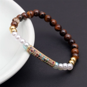 Detail of tiger eye and pearl beaded bracelet with a colorful zircon gold cylinder