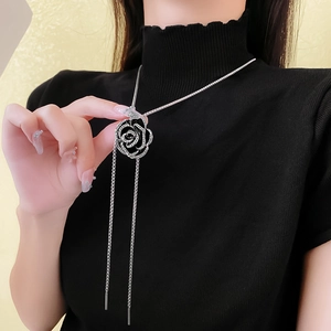 Close-up of a silver black camellia pendant necklace with tassels on black clothing