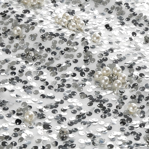 Dettaglio di paillettes argento e perle bianche cucite su un tessuto a rete bianca
