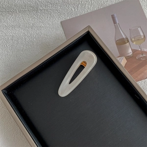 Close-up of a minimalist cream square hair clip on a black textured jewelry tray
