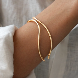 Detail showing the double-layer wavy gold open bangle worn on a model's wrist