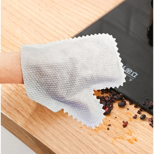 Detail showing white textured non-woven cleaning glove with jagged edges on a wooden table