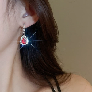 Close-up of elegant gold earrings with red teardrop stones and tassel chains on a model