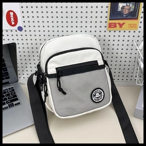 Close-up of white crossbody bag with mesh pocket and black strap on desk background