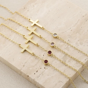 French style gold cross bracelets featuring round cut birthstones on marble surface